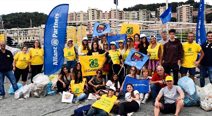 A group of Allianz Partners employees in yellow shirts holding blue and yellow flags, promoting World Clean Up Day and reducing plastic.