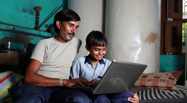 A man and a boy sitting on a bed with a laptop, looking for healthcare access to families in India.