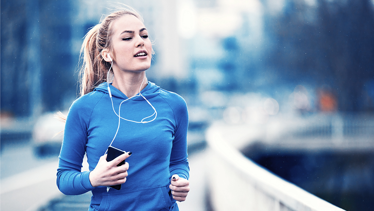 A woman jogging in the city with earphones, enjoying her workout and listening to music.