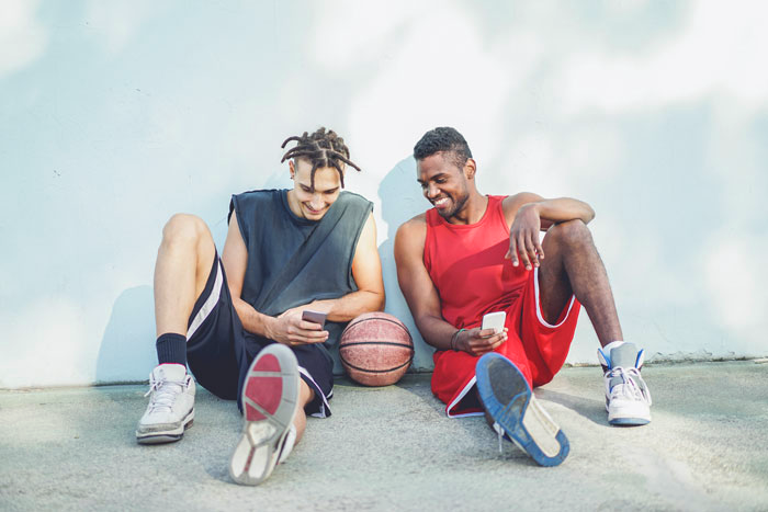 Two young men sitting on the ground, engaged in a game of basketball.