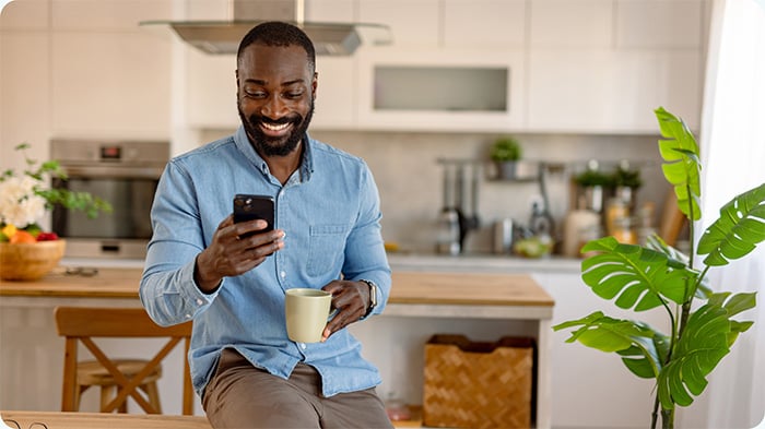 Hombre utilizando su teléfono móvil mientras toma una taza de café