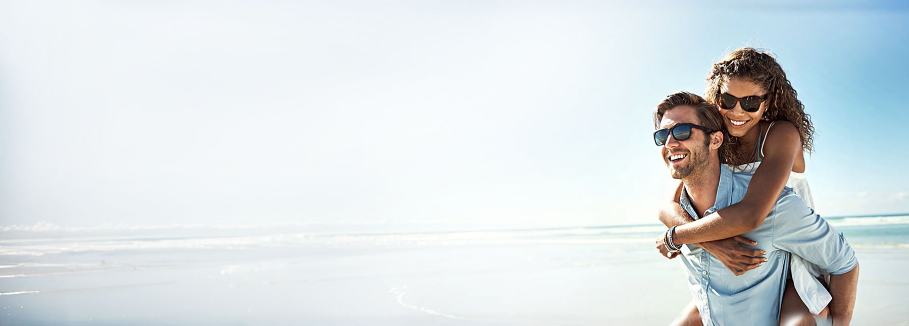 A woman on a mans shoulder walking down a beach.