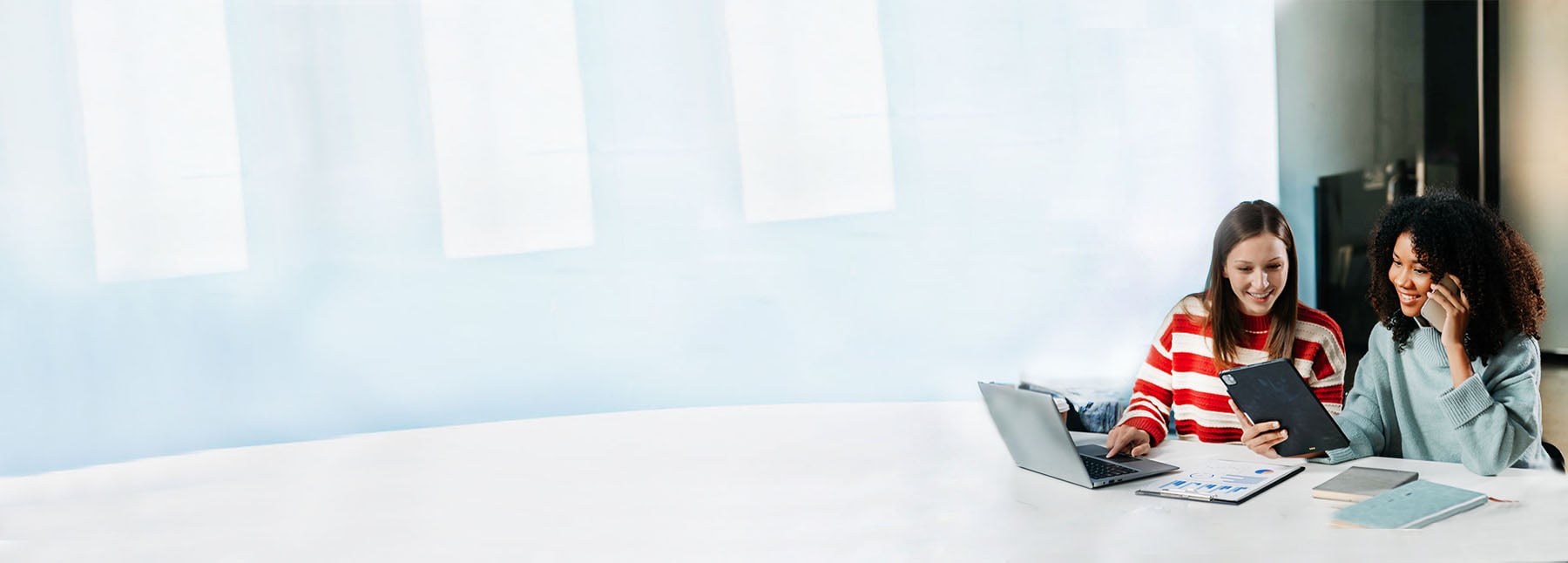 Two woman working on a laptop and phone